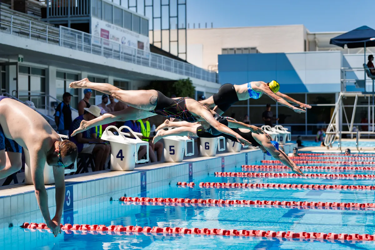 Swimmers diving off the blocks at Pride Swim Carnival